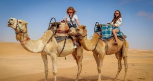 Tourist enjoying their ride on a camel in desert sand.