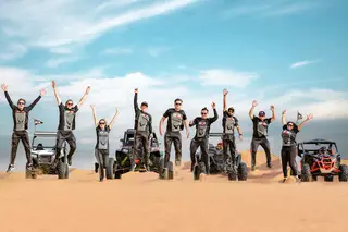 Group of tourists jumping in excitement with off-road buggies on Dubai desert dunes