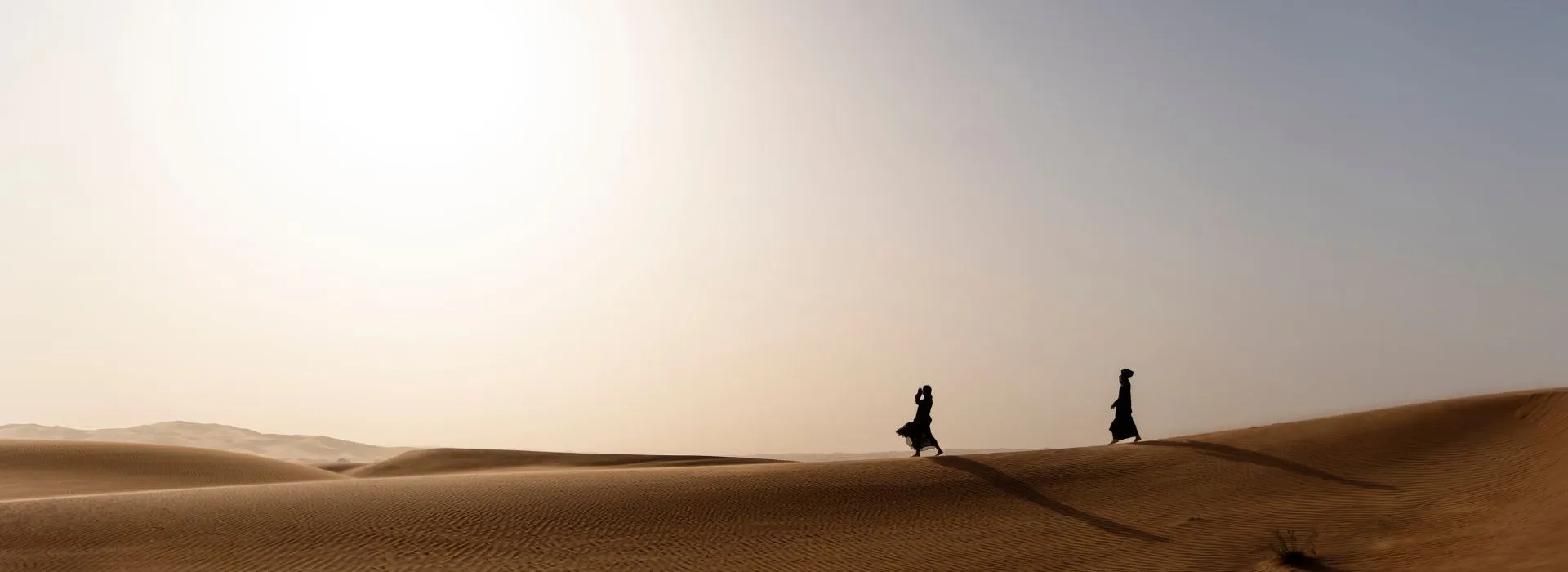 Silhouettes of people walking across sand dunes in the Dubai desert during sunset