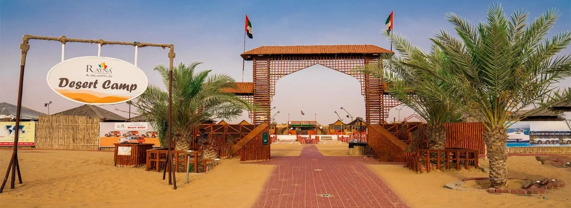 Entrance view of Rayna Desert Camp in Dubai with traditional wooden arch, palm trees, and UAE flags